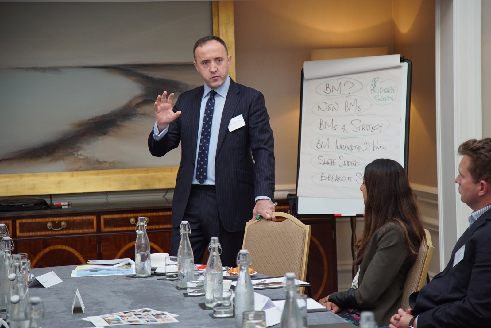 Thomas C. Lawton speaking in a boardroom workshop, standing beside a flipchart, with participants seated in the foreground.
